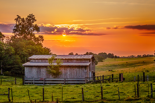 Barn in field with fence with bright orange sunrise sky and purple clouds