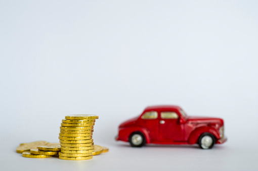 A stack of shiny yellow coins on a background of red retro car on a light gray background. Copy space.
