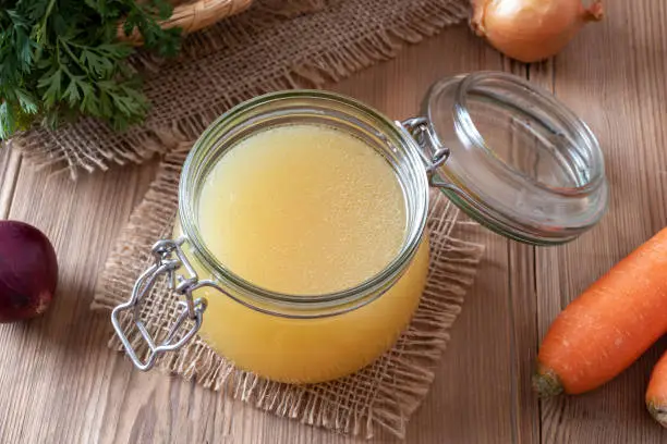 Chicken bone broth in a glass jar and fresh vegetables