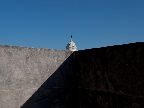 US Capitol building seen behind concrete wall with dark shadow and blue sky