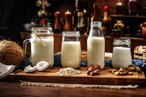 Non-dairy variety of non-dairy milks: Coconut, Oats, Hazelnuts and almonds in drinking glasses. Placed on a table in old fashioned kitchen