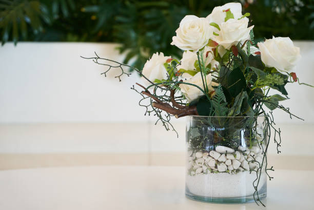 Decorative white roses in a glass vase, close-up. Wedding, valentines day and romantic decoration flowers with exotic plant green leaves on background with copy space.