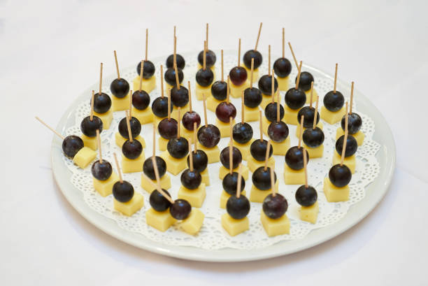 Canape with cheese and grape on plate over white background. Cheddar cheese with grapes on wooden skewers, close-up. Banquet service. Catering food, wine snacks
