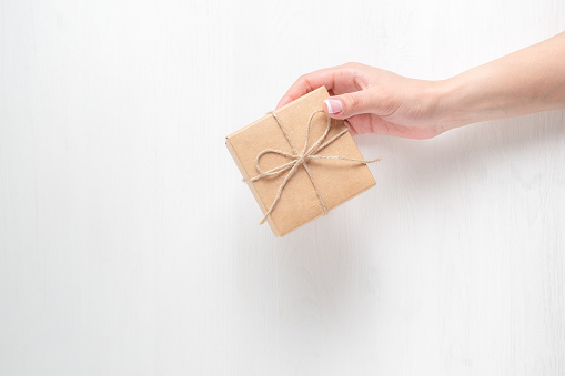 hand of a young girl holding a gift box on a white wooden background