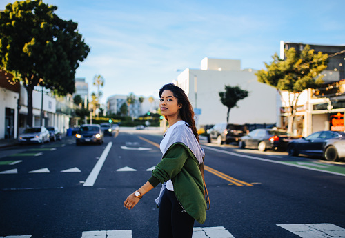 Young mixed Latina woman enjoying the walk on the streets of Santa Monica, Los Angeles. She is wearing a fashionable spring jacket, going to meet her friends near the beach.