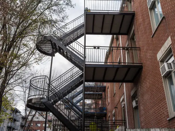 Photo of Fire escape stairs and ladder, in metal, on a typical North American modern residential brick building from Montreal, Quebec, Canada. These stairs, made for emergency, are symbolic of the architecture