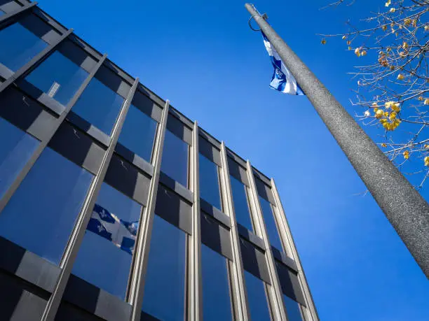 Photo of Quebec flag reflecting in a business financial skyscraper tower waiving in the air. Also known as Fleur de Lys, or fleurdelise, it is the official symbol of the Canadian province of Quebec