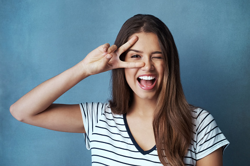 Studio shot of an attractive young woman looking through her fingers against a blue background