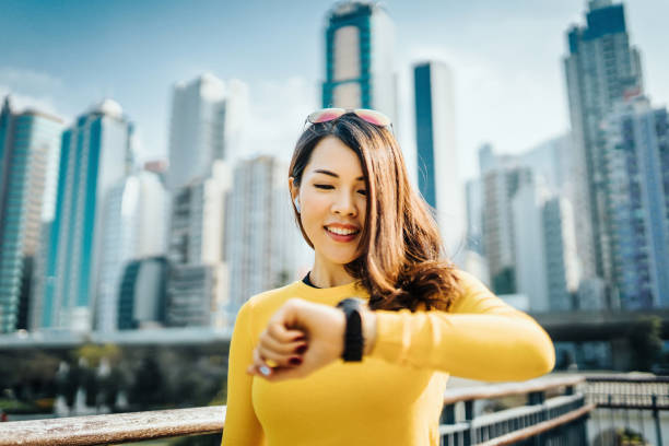 beautiful young sports woman checking smartwatch while exercising outdoors against urban cityscape - self improvement audio imagens e fotografias de stock