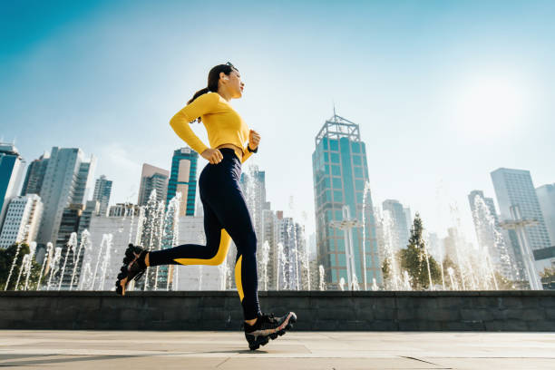 jeune jogger femelle fonctionnant dans le parc urbain dans la ville, avec l'horizon moderne de ville comme fond - running jogging asian ethnicity women photos et images de collection