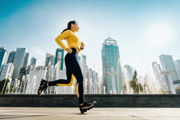 giovane jogger donna che corre nel parco urbano della città, con lo skyline moderno della città come sfondo - running jogging asian ethnicity women foto e immagini stock
