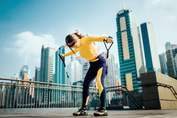 young asian sports woman exercising with a resistance band outdoors, with urban city skyline as background - self improvement audio imagens e fotografias de stock