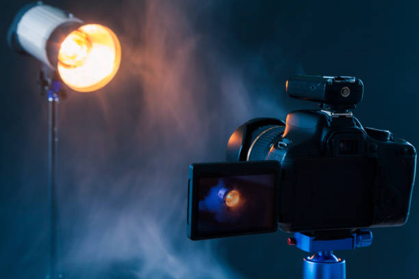 photo de la caméra sur un trépied bleu qui photographie dans le studio un dispositif d'éclairage professionnel dans la fumée. lampes de studio et matériel de fumée. caméra avec synchroniseur radio - high standard photos et images de collection