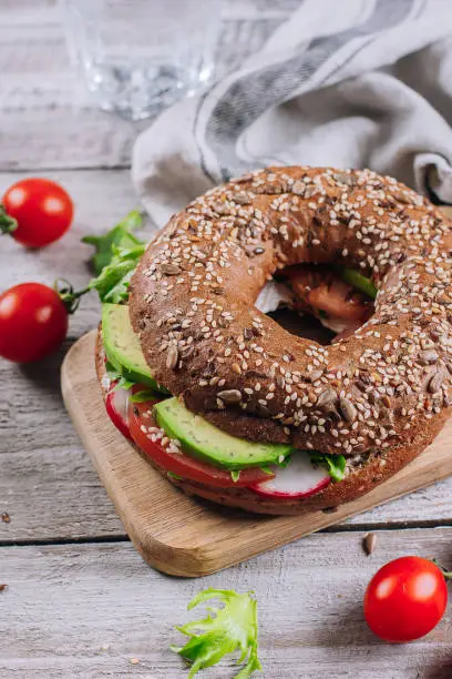 Bagels with cream, avocado, tomatos, radish and green leaves on wooden board and table background. Healthy breakfast food. Delicious balanced food concept. Top view and Copy space