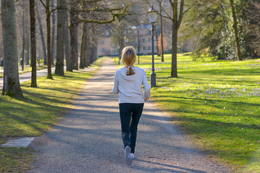 Attractive mature woman taking her daily jog through a wooded park going away the camera along a tree lined avenue in a health and fitness concept