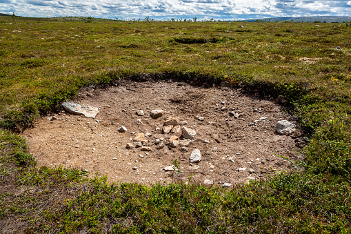 Flat highland landscape view of a large hole in the ground surrounded by green vegetation. Horizontal composition.