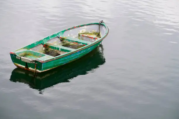 One single green rustic wooden boat alone in sea water uk