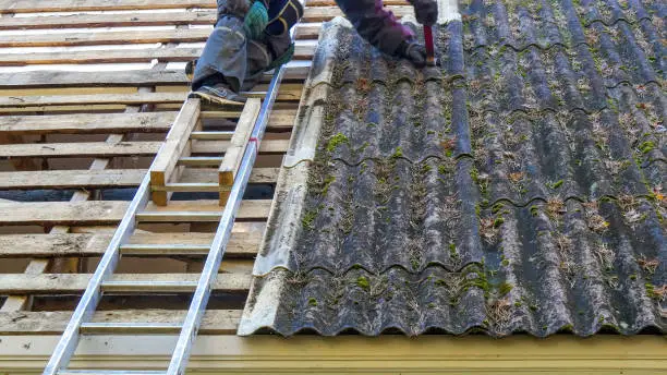 A roofer on the ladder getting off the roofplate on the roof. Sliding down the plate then other roofer catches it
