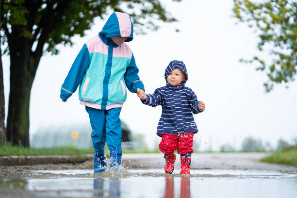 istock children in rain outfits walking through water puddle together 1133352376