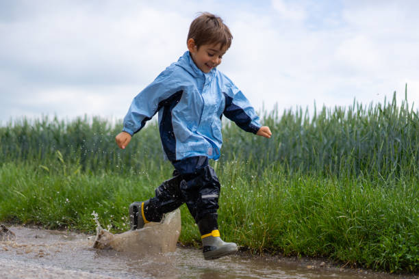 istock little boy in rain clothes running through water puddle 1133352392