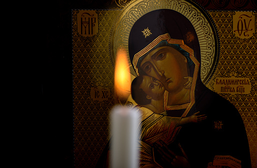Icono ortodoxo de la madre de Dios y el niño Jesús y una vela ardiente borrosa delante del icono photo