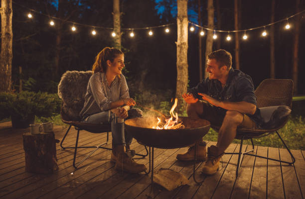 Love summer night Young couple on vacation in countryside, they enjoy in summer nature. sitting on porch next to the fireplace, drinking coffee and have romantic sunset glamping photos stock pictures, royalty-free photos & images