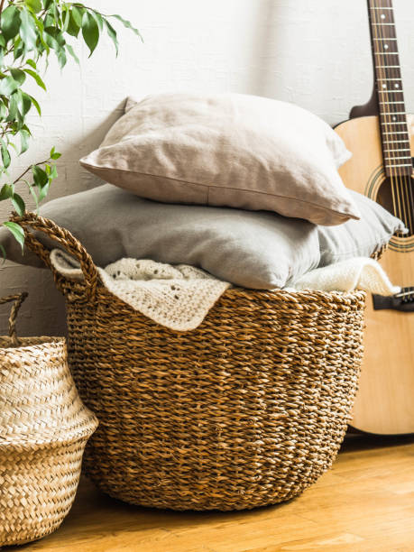 Wicker basket with gray cushions, houseplant and guitar on floor near a white wall stock photo