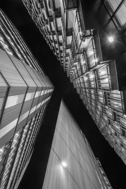 Highly detailed abstract wide view up towards the dark night sky from a very low angle in the financial district of London City and its ultra modern contemporary buildings. Monochrome edit in Black and White image with high contrast ideal for background.