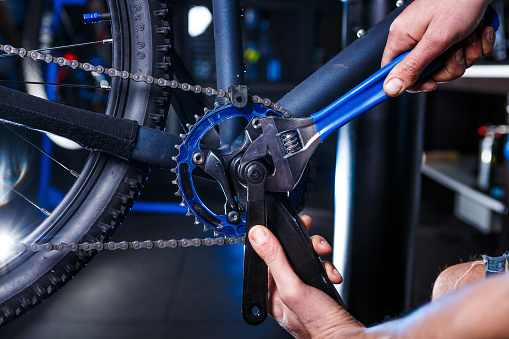 A close-up of a male bicycle mechanic's hand in the workshop uses a screwdriver tool to adjust and repair the bicycle crank assembly, the front bike stars in the bicycle store