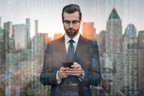 istock Chat with client. Handsome young businessman in suit using smartphone while standing against of cityscape background. 1133374448