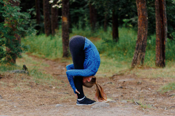 istock Girl in blue sportswear doing exercises outdoors in coniferous forest. Standing forward fold. Healthy lifestyle sport concept. 1133374576