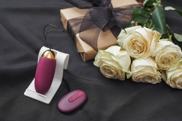 Valentine's Day gift ideas. CLose up of purple vibrating egg with remote and beautiful white roses stock photo
