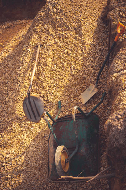 riempimento dello scavo sotto la lastra di fondazione. costruzione, dolomite, pale e carriola. - scaffolding wheel construction site metal foto e immagini stock
