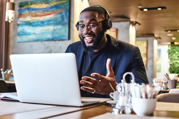 travaillez jusqu'à ce que vous n'ayez plus besoin de vous présenter. jeune homme d'affaires avec le casque s'asseyant dans le café devant l'ordinateur portatif et le réseautage - no audio photos et images de collection