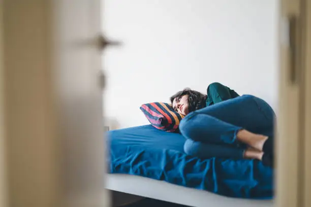 Lonely young woman is laying on bed alone in room