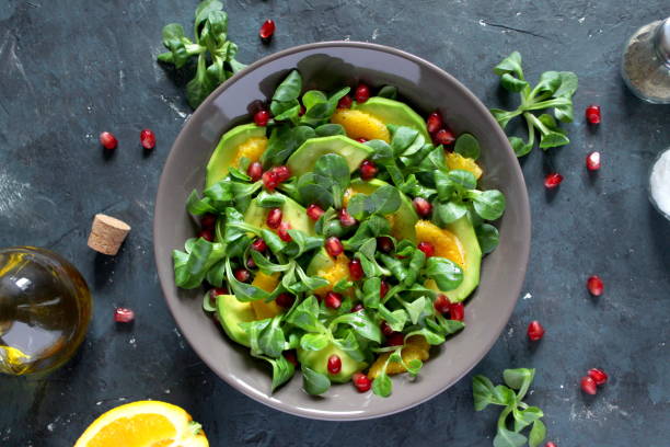Green salad with avocado, orange and pomegranate in a bowl over dark background. stock photo