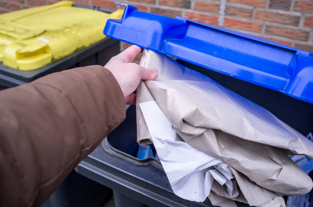 istock Male hand throws old paper into a trash can with a blue lid. Waste sorting. The concept of saving attitude to the environment. 1133388234