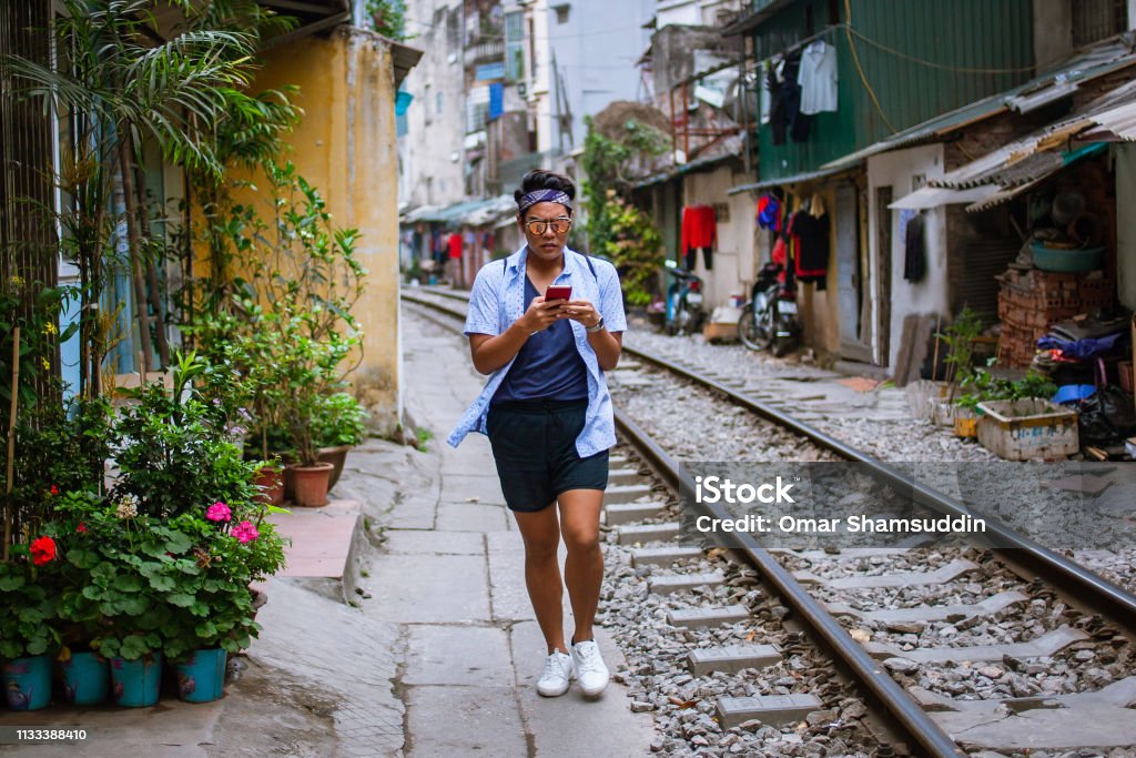 Asian guy walking by railroad track with smartphone in narrow alley in Hanoi Walking in Old Quarter, Hanoi, Vietnam. Vietnam Stock Photo