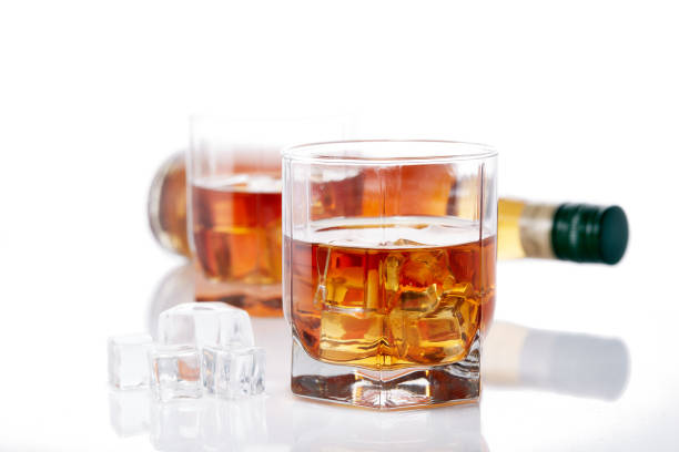 Bottle of whisky and two glasses of whisky with ices on a white background with reflection