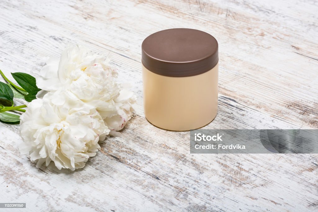 Body and hair cosmetics, peonies on wooden background Beige mocap can for cream after skin care face and body and flowers peonies lying on a battered texture light wooden table, view directly, close-up. View directly, space for text. Beauty Stock Photo