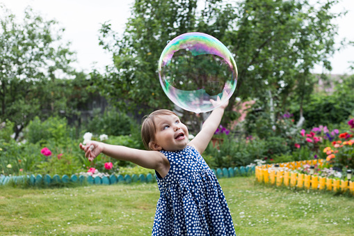 Pretty little girl is playing with big bubbles in a park.