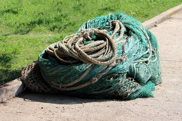 Various Types Of Heavily Used Fishing Nets And Strong Ropes With Rusted  Chains On One Large Pile On Edge Of Sidewalk Next To Uncut Grass In Local  Park Stock Photo - Download