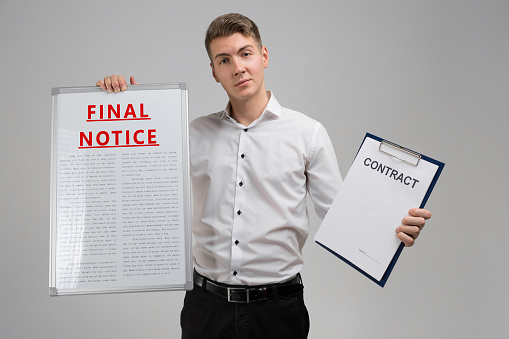 man in a shirt with a poster with a red inscription about final notice and contract isolated in a bright Studio. Holding Invoice With Final Demand Notification. FINAL EXAM message on the card shown by a man