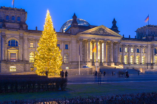 Illuminated Christmas tree in front of Reichstag building in Berlin is captured in the winter evening. The scene looks festive and atmospheric.