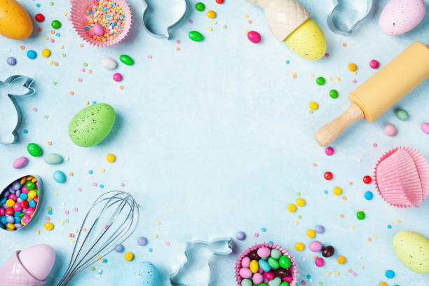 Easter baking background with rolling pin, whisk, decorative eggs, cookie cutters, candy and colorful confetti on kitchen table top view. Flat lay.