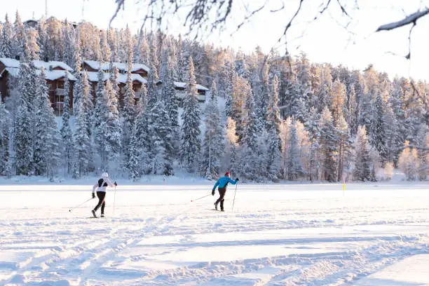 Two athletes running on skis on a frozen lake against the snow-covered forest.   Lapland Finland Ruka