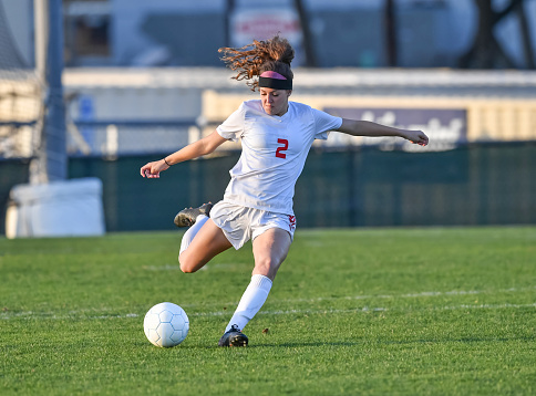 Very athletic young girl kicking and dribbling the soccer ball on a grassy green field.