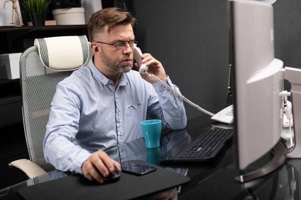 istock Serious Businessman working in office at computer Desk and talking on landline 1133404545