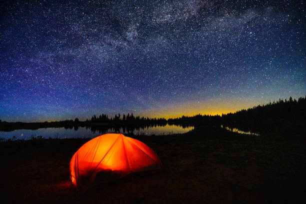 Tent Camping at Backcountry Mountain Lake - Scenic wilderness lake with orange glowing tent with stars and night sky.