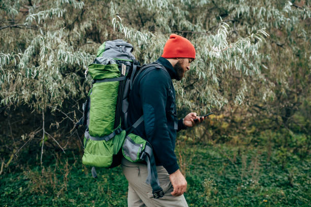 istock Side view shot of young handsome hiker male using cellphone for GPS application, in red hat and travel equipment. Traveler bearded man trekking and mountaineering. Travel, people and lifestyle concept 1133416659